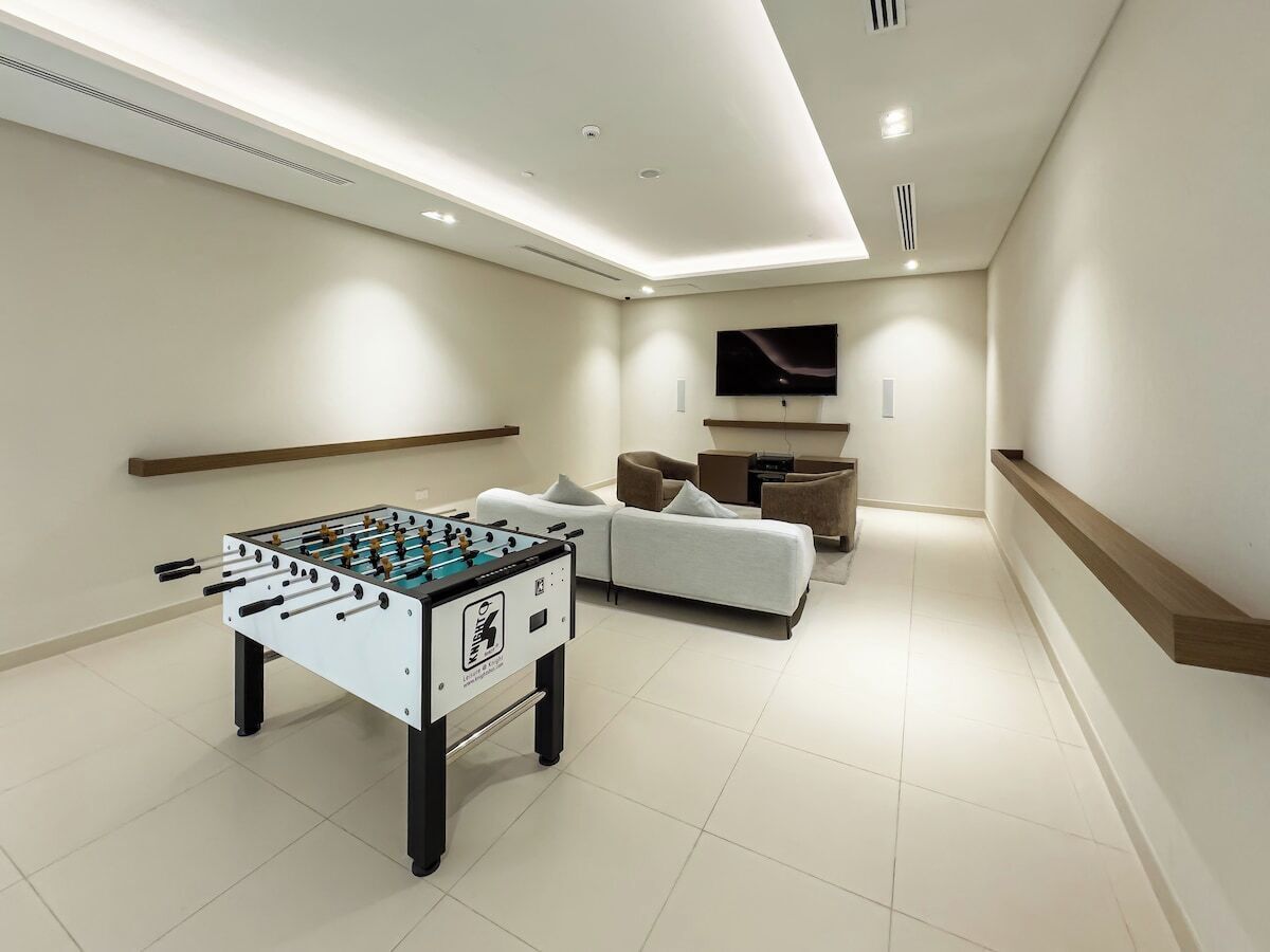Un salon moderne avec une table de baby-foot, un canapé et un téléviseur à écran plat fixé au mur.