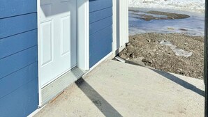 A coastal building with a white door, a concrete porch, and a view of the ocean. - Complexe Étoile d'Or (Riviere à Claude)