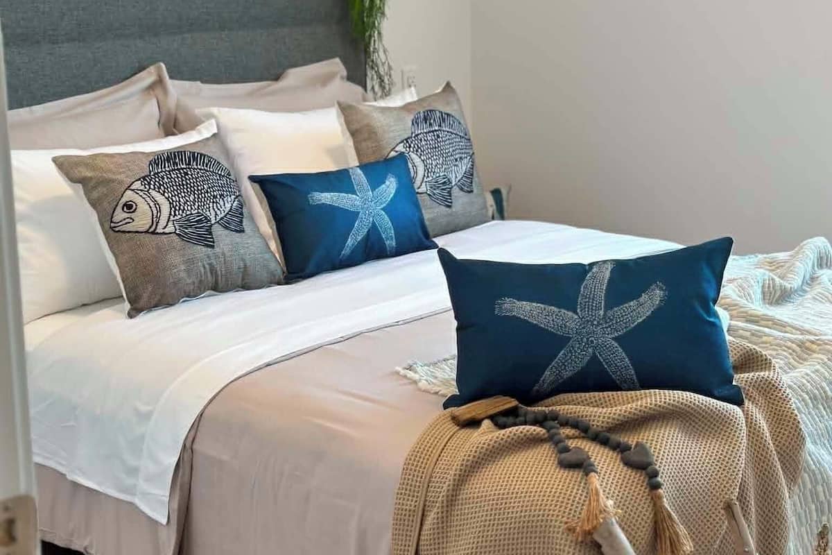 A neatly made bed with a headboard, multiple pillows, a woven throw blanket, and a hanging light fixture.
