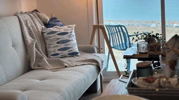 A living room with a sofa, a lamp, a table with plates, and a view of the sea. - Complexe Étoile d'Or (Riviere à Claude)