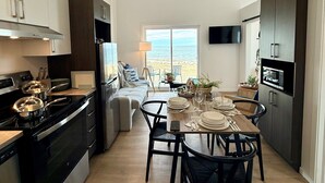 A modern kitchen with a dining area, a TV mounted on the wall, and a view of the sea through a large window. - Complexe Étoile d'Or (Riviere à Claude)