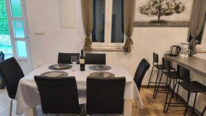 Ein Essbereich mit Tisch für zwei Personen, Stühlen, einem Fenster mit Vorhängen, einem an der Wand montierten Lichtschalter und einer Kaffeemaschine auf der Arbeitsfläche.