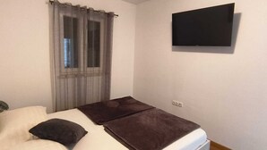 Ein Schlafzimmer mit einem Bett, einem an der Wand montierten Fernseher und einem Fenster mit durchscheinenden Vorhängen.