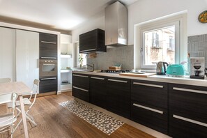 Eine moderne Küche mit dunklen Schränken, einem eingebauten Backofen und einem Fenster mit Blick auf eine Stadtlandschaft.