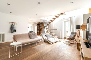 Ein modernes Wohnzimmer mit einer Couch, einem kleinen Tisch, einem Schaukelstuhl, einer Treppe und einem Fernseher.