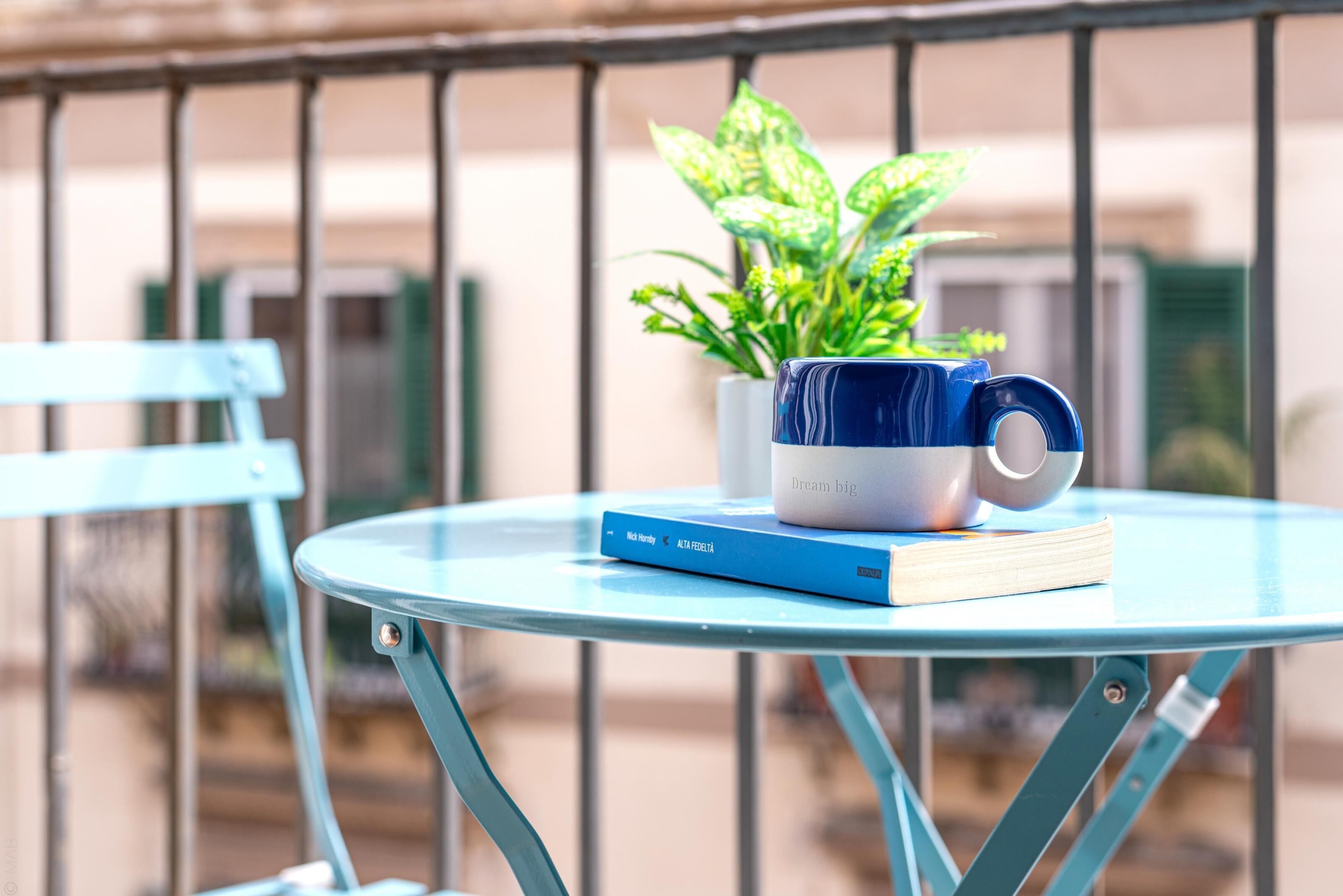 A blue table with a book and a mug on it, a potted plant, and a blue chair.