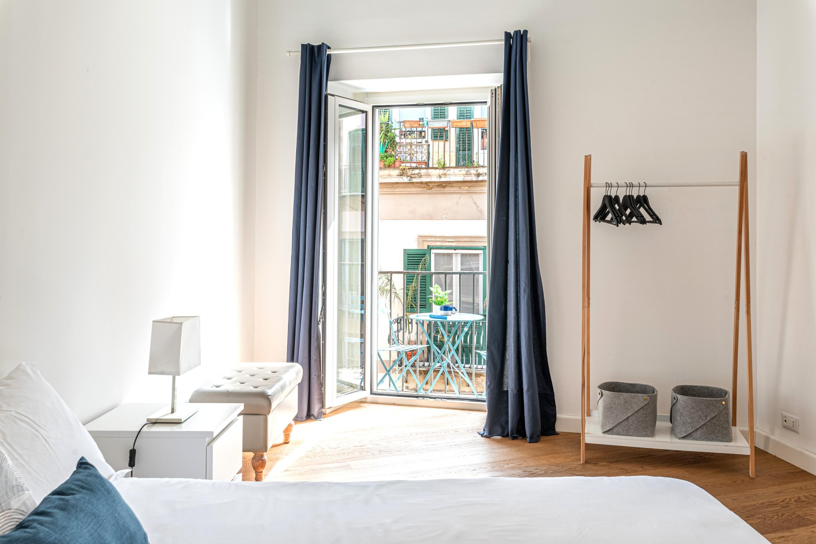 Une chambre à coucher comprenant un lit, une table de chevet, une lampe et donnant sur un balcon extérieur.