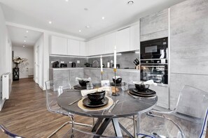 A modern kitchen with white cabinets, a built-in oven, and a dining area with a glass table and chairs. - Fantastic 2 bed Flat with amazing view in Barking (Barking)