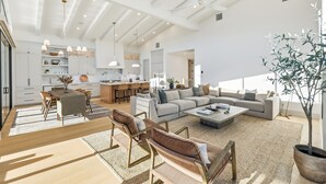 A spacious living area with a large sofa, a dining table, and chairs. There is a kitchen in the background with modern appliances and cabinets. - Lake Luxury- Juniper Ridge-Pool Table and Beautiful Decor (Graford)