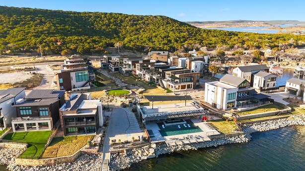 A modern residential area with contemporary houses, a central pool, and a view of a lake and forested hills. - Lake Luxury- Juniper Ridge-Pool Table and Beautiful Decor (Graford)