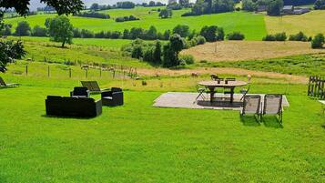 Un espace extérieur verdoyant, avec une table et des chaises, entouré d’arbres et offrant une vue sur un paysage verdoyant.