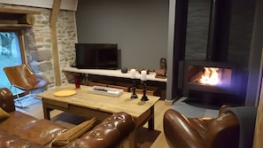 Een gezellige woonkamer met een stenen muur, een flatscreen televisie, een open haard, lederen meubels en een houten tafel.