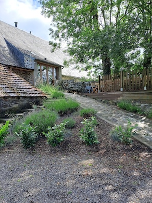 Un bâtiment en pierre avec un toit en tuiles, un chemin de gravier et une clôture en bois.