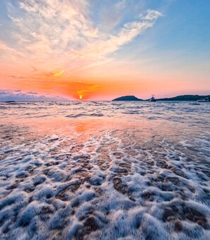 Une plage avec des vagues et un coucher de soleil en arrière-plan.