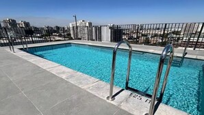 A rooftop pool with clear blue water, metal railings, and a cityscape view in the background. - Family-Friendly Apartment • Walk to Parks & Shops • Safe and comfort for all. (Santiago)