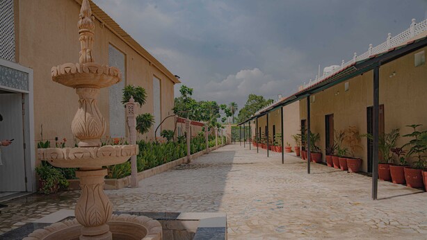 Un patio con una fuente central, plantas en macetas y un camino de baldosas.
