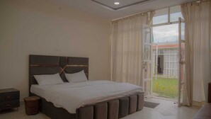 Un dormitorio con una cama grande, una mesita de noche, un cubo de basura y vistas a un jardín por una puerta abierta.