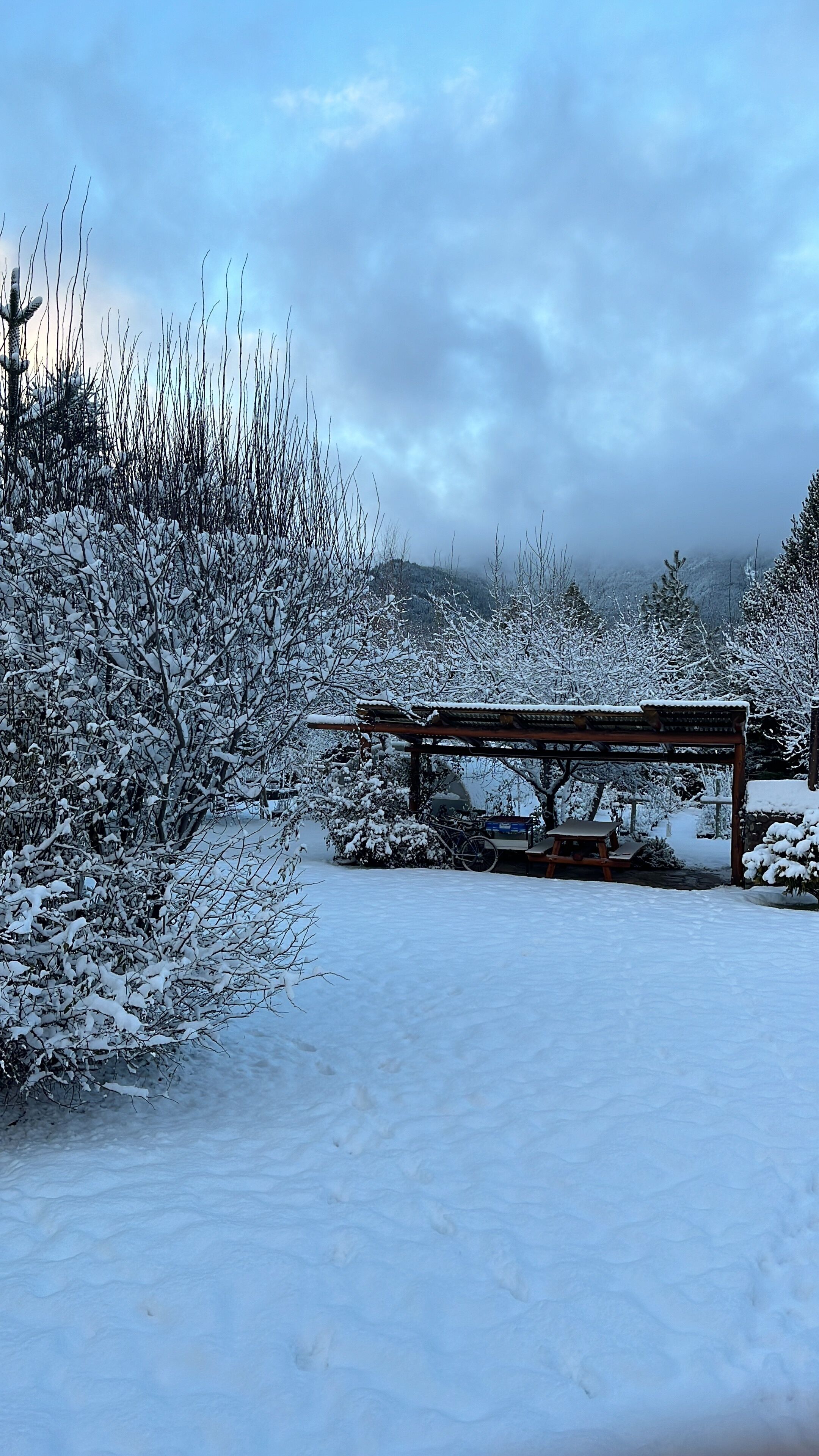 A snow-covered outdoor area with a wooden bench and a covered seating area.