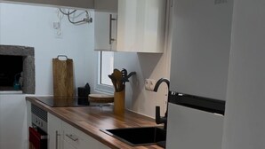 A modern kitchen with white cabinets, a wooden countertop, a built-in oven, and a black refrigerator. - Casa Santa Maria (Vila do Porto)