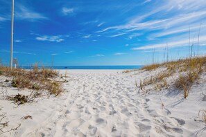 Een zandpad langs het strand, met duinen en een helderblauwe lucht.
