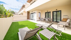 A modern outdoor patio with artificial grass, lounge chairs, and a dining area. - Amalia Garden Groundfloor Retreat, a footstep from beach and sea, By OYOOSTAYS (Torrevieja)
