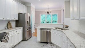 Une cuisine moderne avec des meubles blancs, des appareils en acier inoxydable et une grande fenêtre donnant sur un paysage verdoyant.