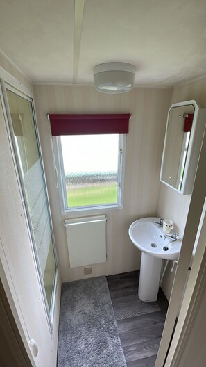 A compact bathroom with a window, a radiator, a sink, and a mirror. - Walsh's Holiday Park - The Sapphire (Skegness)