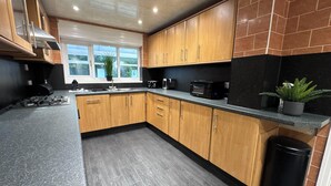 A modern kitchen with wooden cabinets, a gas stove, a sink, and a microwave. - Sandringham & Spa Villa (Lancashire)