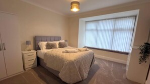 A bedroom with a bed, bedside tables, a wardrobe, and a window with blinds. - Sandringham & Spa Villa (Lancashire)