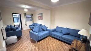 A modern living room with a sectional sofa, a small table, and a lamp. - Sandringham & Spa Villa (Lancashire)