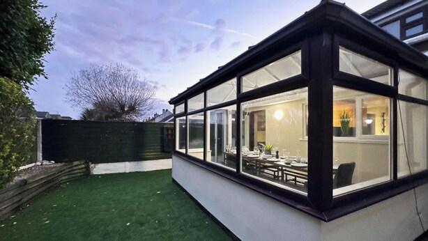 A conservatory with a dining area visible inside, surrounded by a green lawn and a white wall. - Sandringham & Spa Villa (Lancashire)