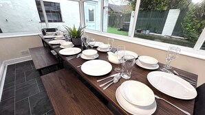 A dining area with a long wooden table set for a meal, surrounded by windows with a view of a backyard. - Sandringham & Spa Villa (Lancashire)