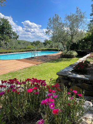 A swimming pool with a wooden deck, surrounded by a grassy area and flowering plants. - Tuscan Farmhouse with pool in the Chianti (Montefiridolfi)