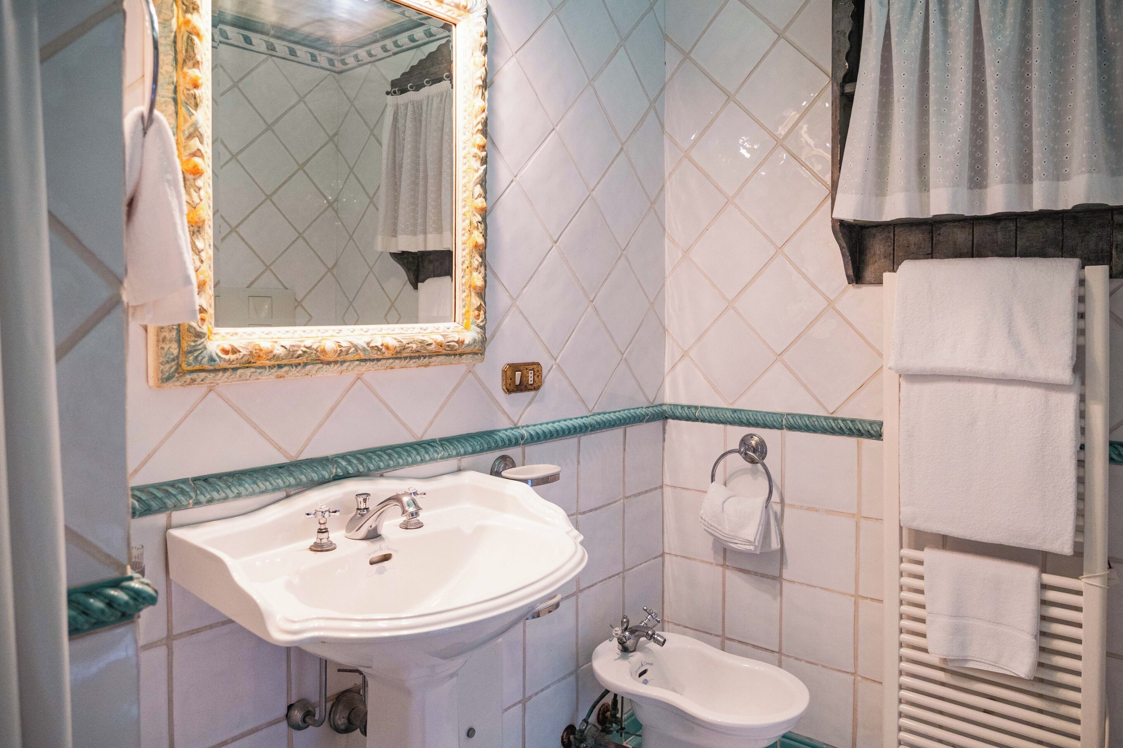 Un baño con lavamanos blanco, un espejo y un perchero para toallas.