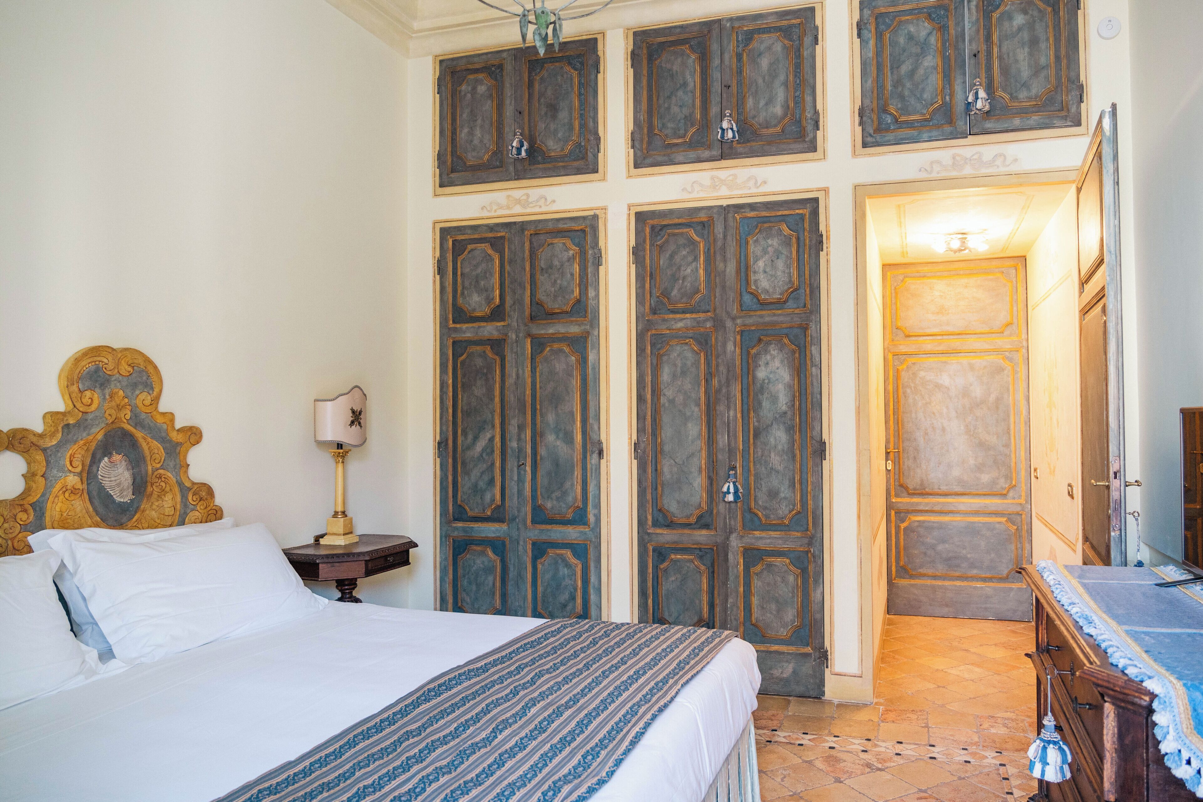 Habitació d'hotel amb un llit, una tauleta de nit, una làmpada i un armari amb diverses portes.