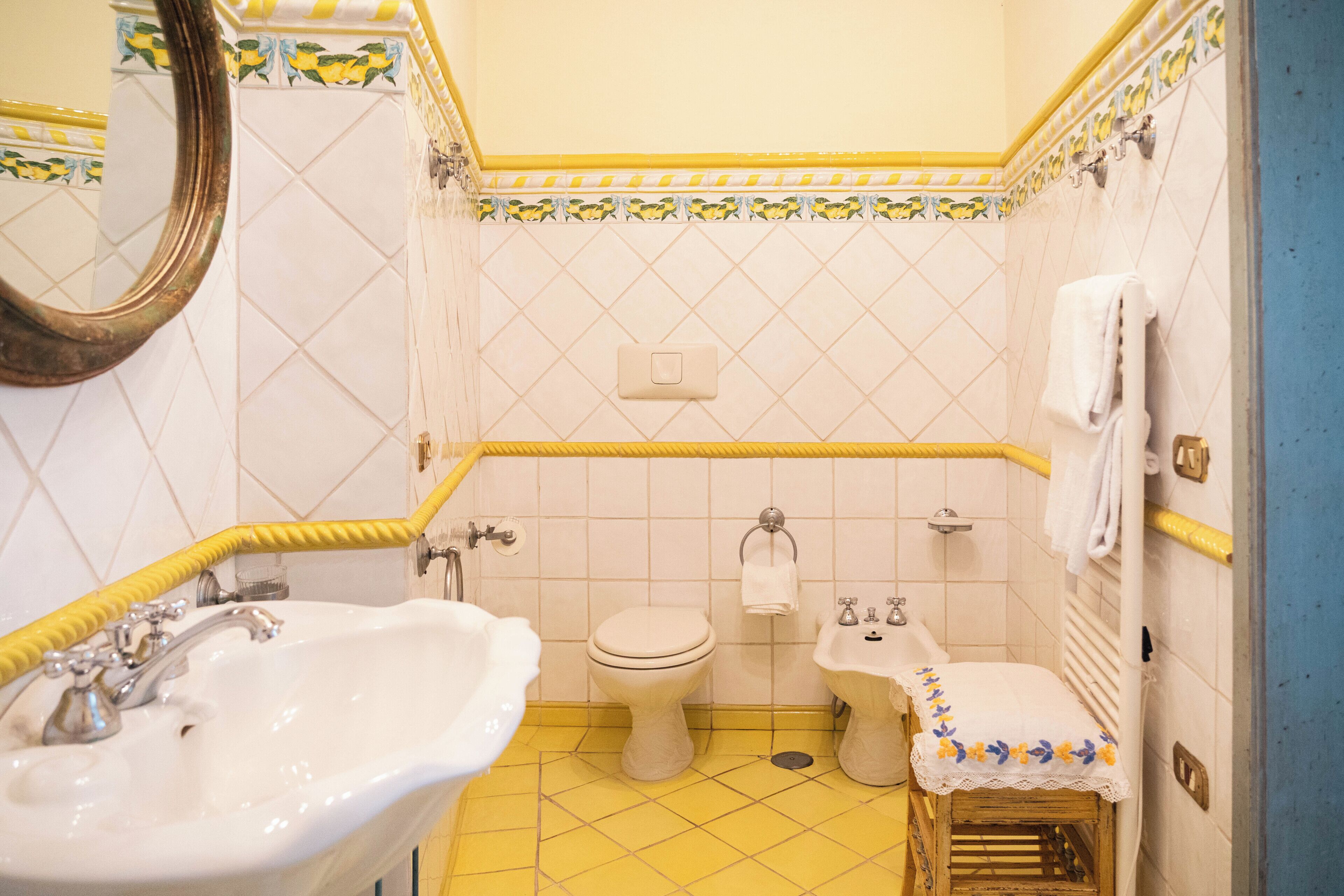Une salle de bain avec un lavabo, des toilettes et un bidet, un sol carrelé de carreaux jaunes et un miroir.