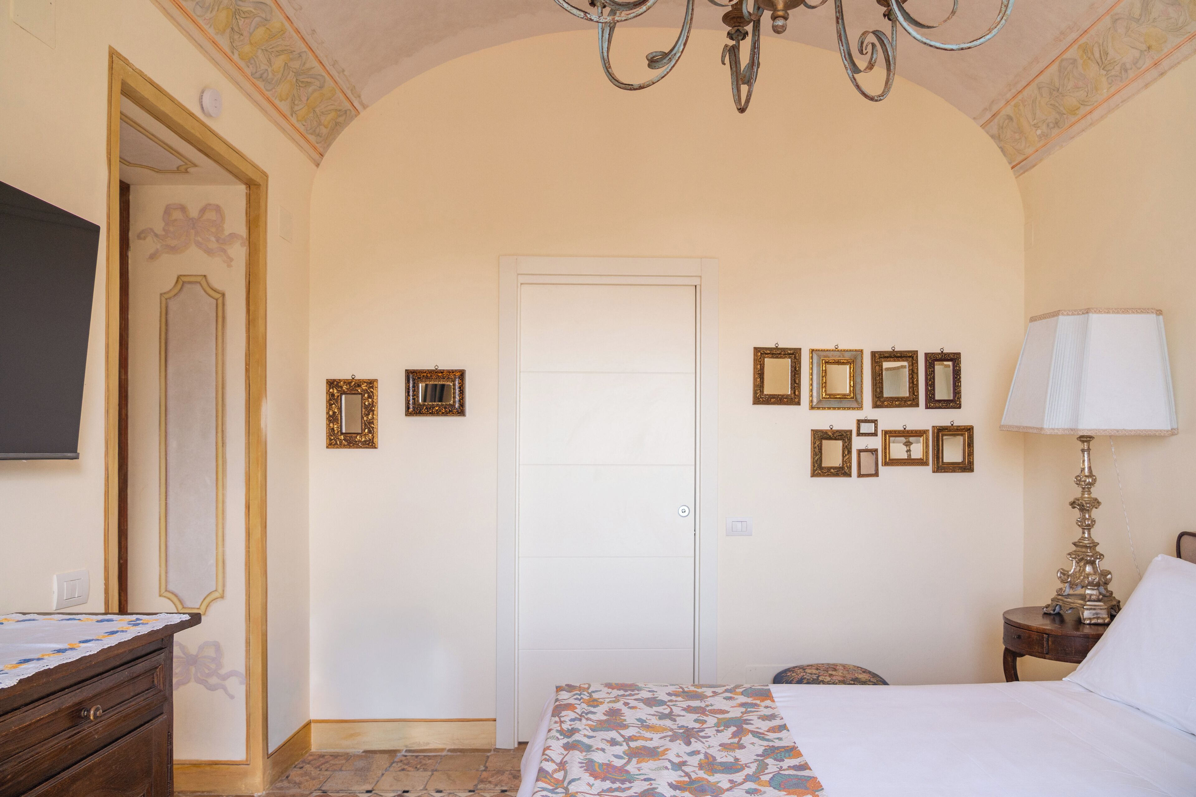 A bedroom with a bed, a dresser, a mirror, a door, and a chandelier.