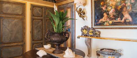 A room with a wooden table, a potted plant, a decorative lamp, and a painting on the wall.