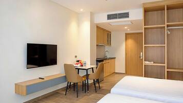 Una habitación de hotel con cama, televisor montado en la pared, una kitchenette pequeña y un armario de madera.