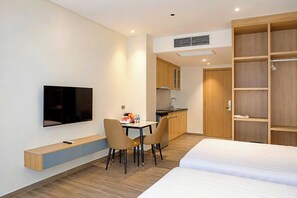 Une chambre d’hôtel avec un lit, un téléviseur fixé au mur, une petite kitchenette et une armoire en bois.