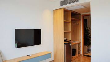 Una habitación moderna con un televisor de pantalla plana montado en la pared, un armario de madera con las puertas abiertas y un pequeño banco con un control remoto.