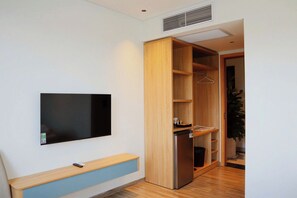 Une chambre moderne avec un téléviseur à écran plat fixé au mur, une armoire en bois dont les portes sont ouvertes, et un petit banc sur lequel se trouve une télécommande.