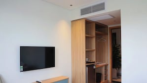 Une chambre moderne dotée d’un téléviseur à écran plat fixé au mur, d’une armoire en bois dont les portes sont ouvertes, et d’un banc muni d’une télécommande.