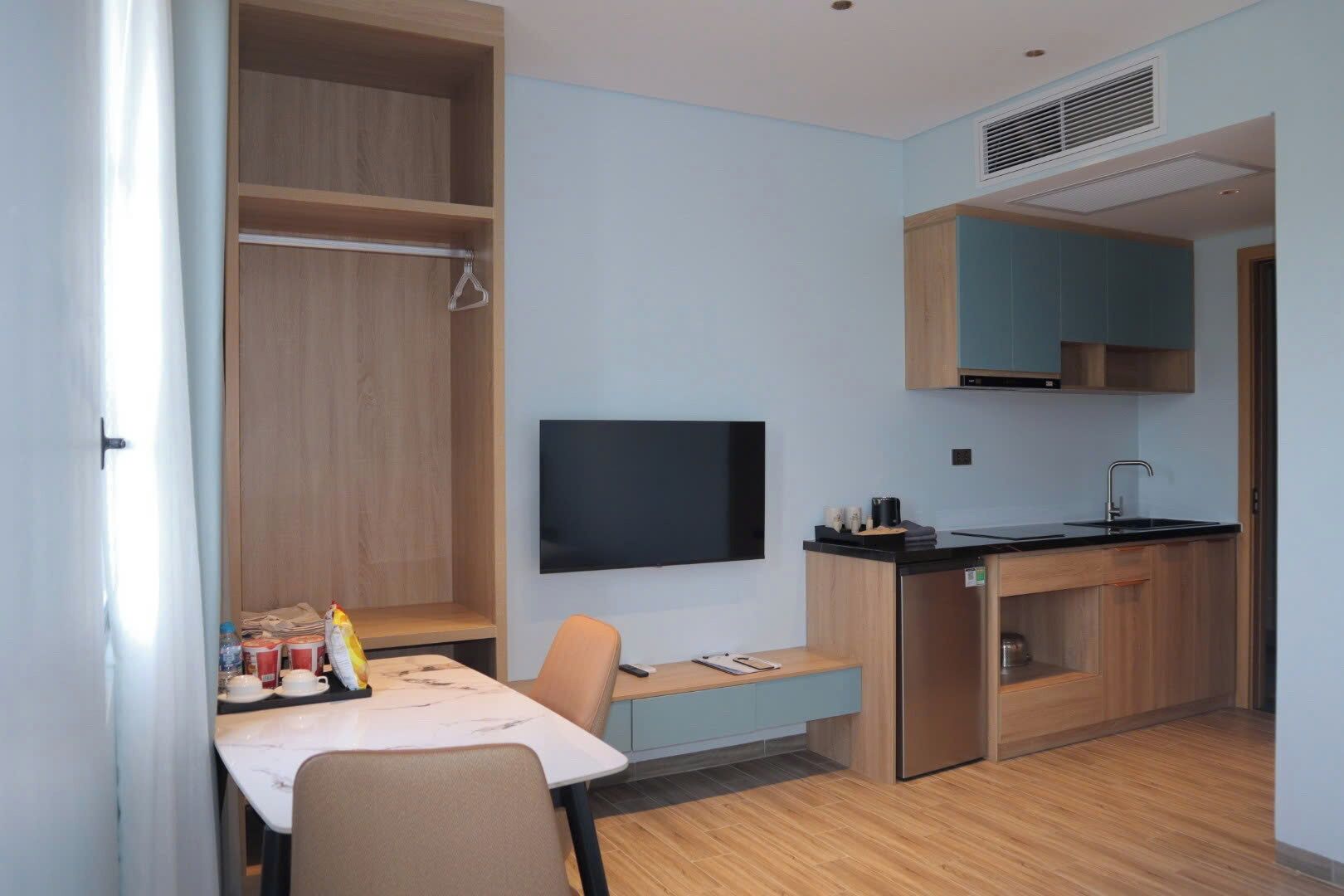 A compact kitchen with a built-in oven, a small dining area with a table and chairs, and a TV mounted on the wall.