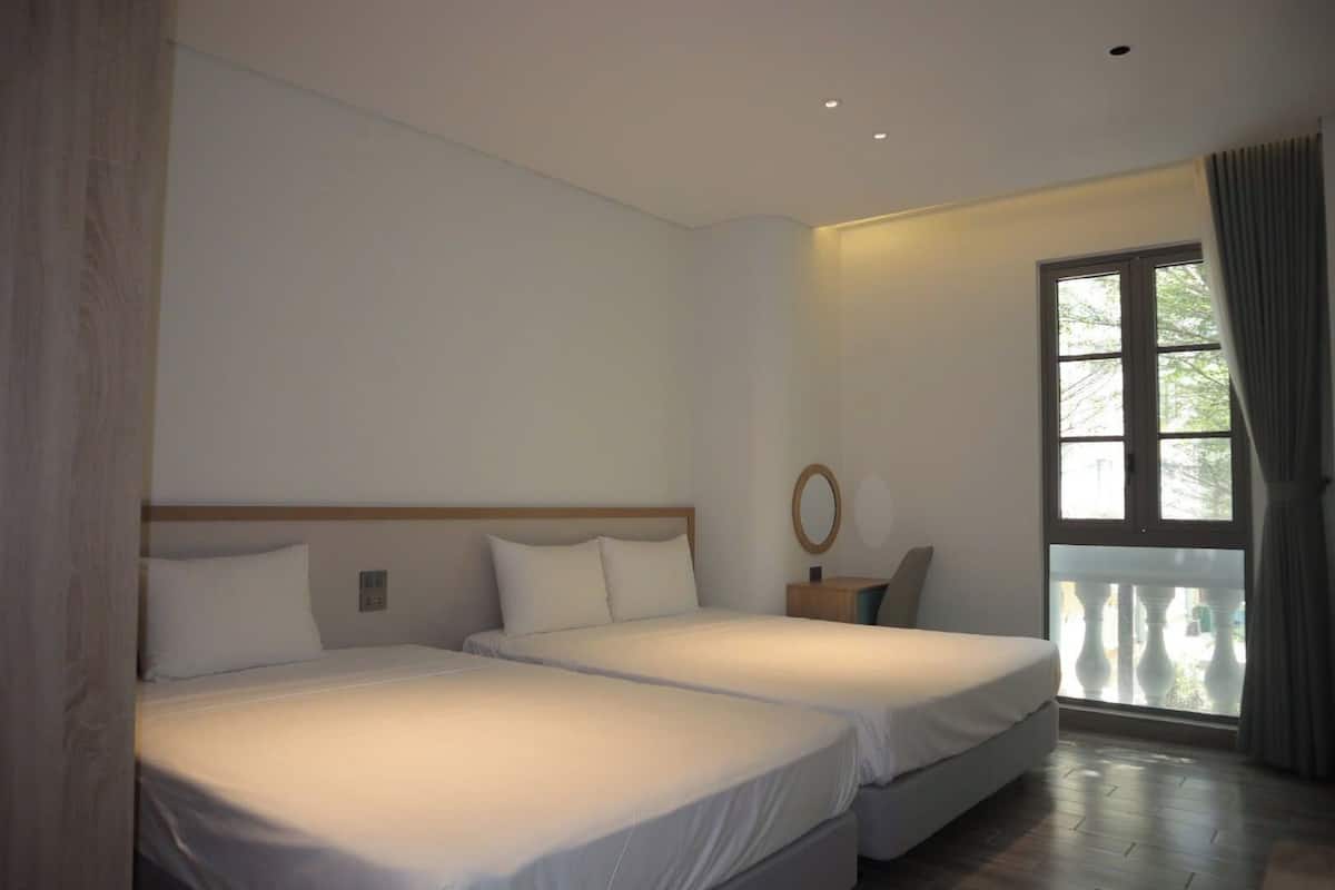 Una habitación de hotel con dos camas, un ventanal con cortinas y una mesita de noche pequeña.