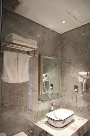 A bathroom with a marble wall, a glass-topped sink, a towel rack, a mirror, and a hairdryer. - Sora Hotel (Phu Quoc)