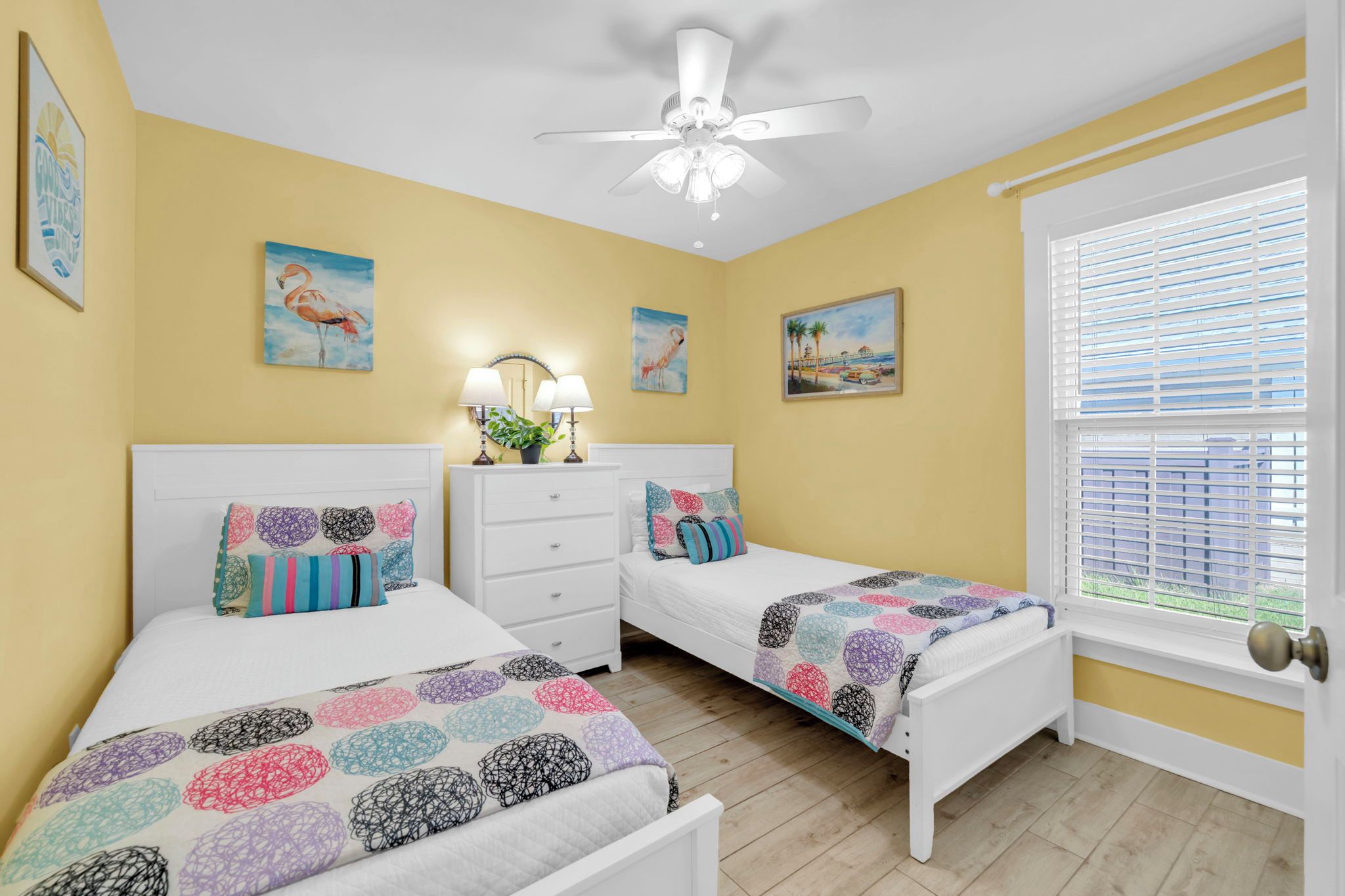A bedroom with two beds, a ceiling fan, and artwork on the walls.