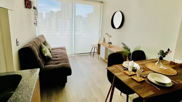 Una sala de estar moderna con sofá, mesa de comedor, sillas y un ventanal con persianas.
