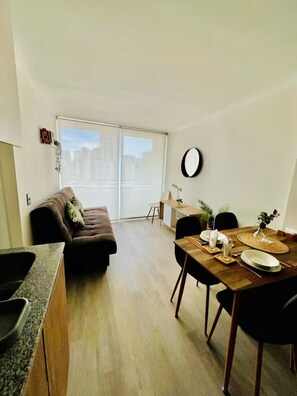 A modern living room with a sofa, dining table, chairs, and a large window with blinds. - Beautiful and comfortable apartment in an excellent location: R11-1   (Santiago)