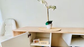 Un espacio de trabajo minimalista con un escritorio de madera, una silla blanca, una orquídea pequeña en maceta y una estantería con una caja etiquetada 'DOMINO'.
